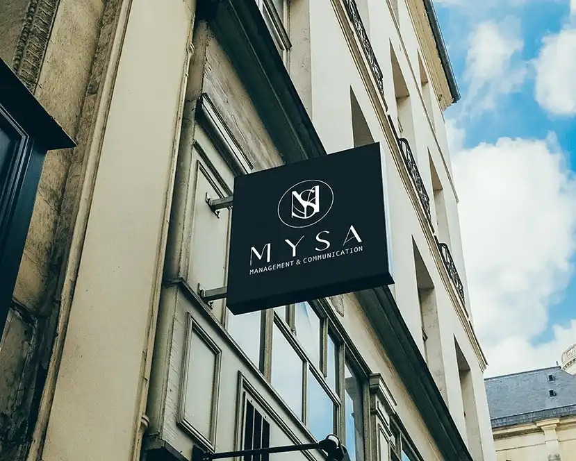 A black MYSA blade sign projecting from the stone facade of a classic European street building
